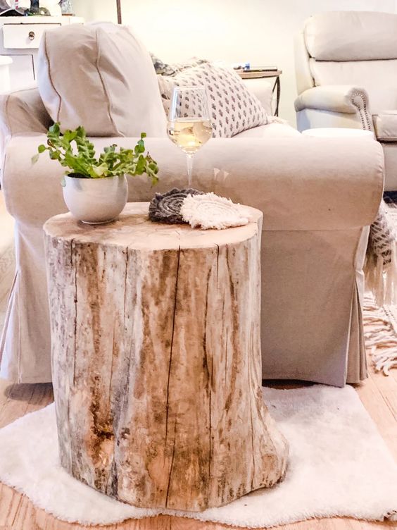 Cozy living room with beige armchair, rustic tree stump side table, potted plant, and a glass of wine on top.