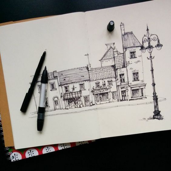 Urban sketch of quaint buildings on open notebook with pen and marker, showcasing architectural drawing skills.