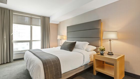 Modern hotel room with a cozy queen-sized bed, stylish decor, bedside tables, and two lamps, featuring a large window.