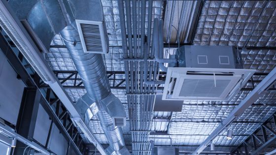 Modern HVAC duct and ventilation system installed in an industrial ceiling, showcasing air conditioning pipes and units.