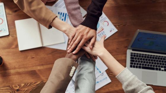 Business team collaboration: diverse group stacking hands over work desk with laptop and charts, emphasizing unity and teamwork.