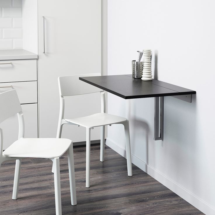 Modern kitchen with white chairs and black wall-mounted foldable table on wooden floor. Space-saving design.