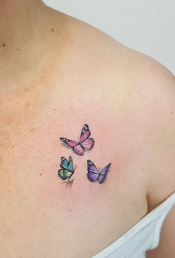 Colorful butterfly tattoo on upper chest, featuring three delicate butterflies in pink, blue, and purple hues.