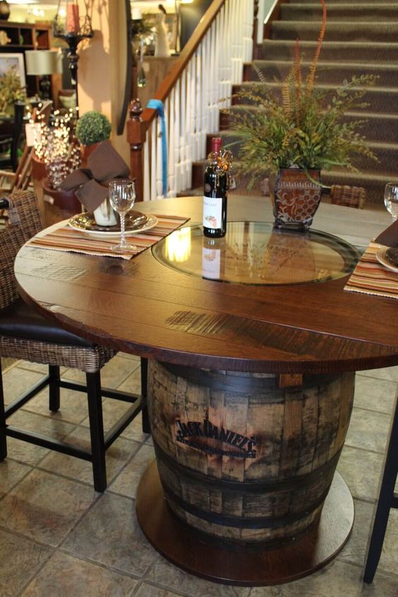 Unique dining table made from a rustic Jack Daniel's whiskey barrel with wine bottle centerpiece and elegant table settings.