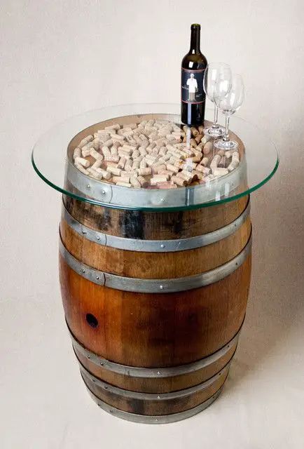 Creative barrel table with glass top, filled with corks, topped with a wine bottle and wine glasses. Unique wine decor.