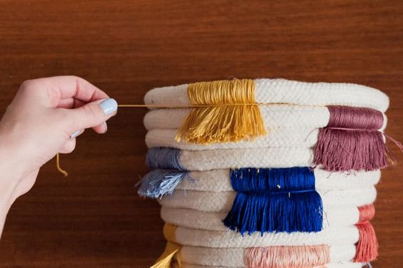 Hand touching multicolored tassels on a woven basket against a wooden background. Craft supplies and decoration.