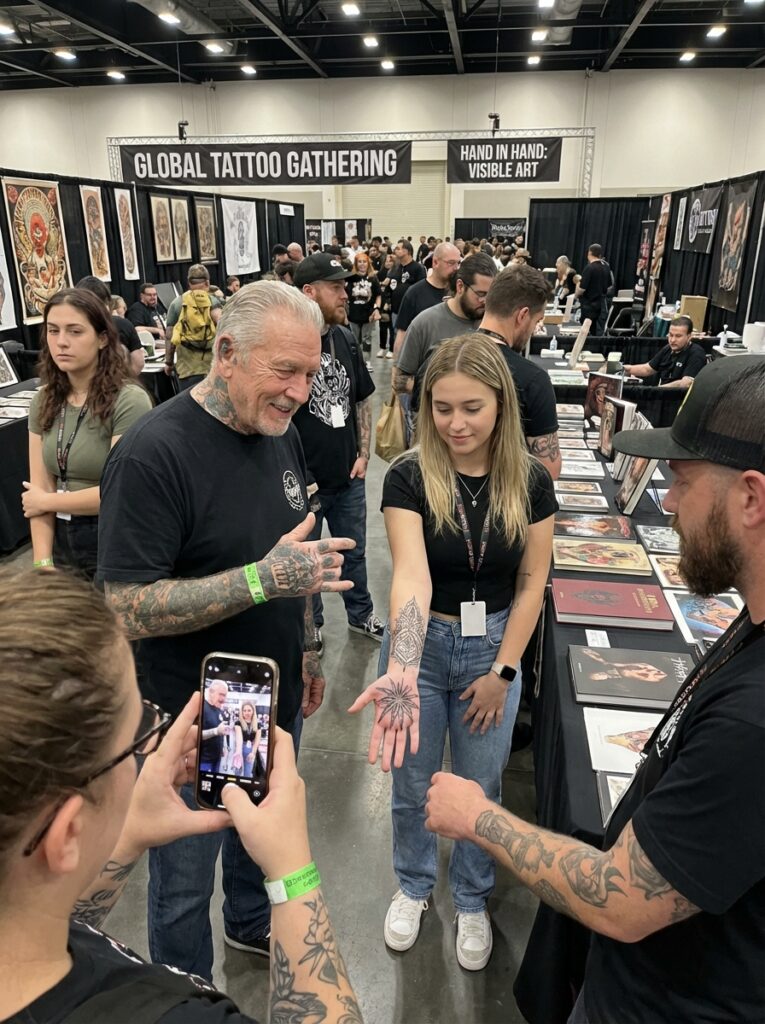 ai-photo-studio-1766759690723-1 Tattoo artist shows intricate blackwork design at the Global Tattoo Gathering, with attendees capturing the moment on their phones. | Sky Rye Design Tattoo artist shows intricate blackwork design at the Global Tattoo Gathering, with attendees capturing the moment on their phones.