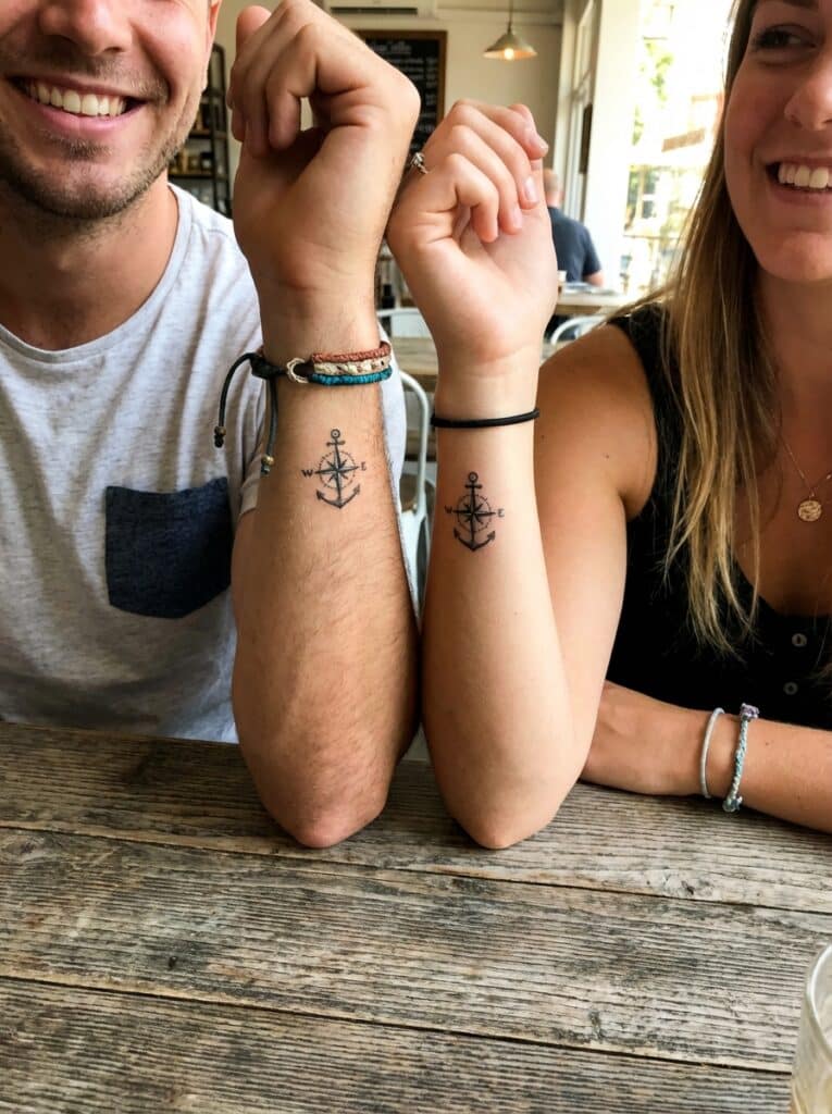 ai-photo-studio-1766760700054-1 Couple showing matching anchor tattoos on forearms in a cozy cafe setting, symbolizing stability and direction. | Sky Rye Design Couple showing matching anchor tattoos on forearms in a cozy cafe setting, symbolizing stability and direction.