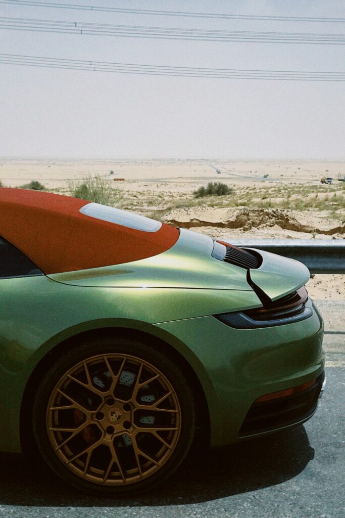 Green sports car with bronze rims and red roof driving through a desert landscape, illustrating luxury automotive design.