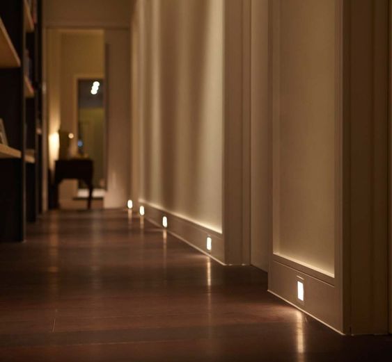 Modern hallway with elegant recessed lighting along dark wooden floors and minimalistic decor, creating a warm and inviting ambiance.