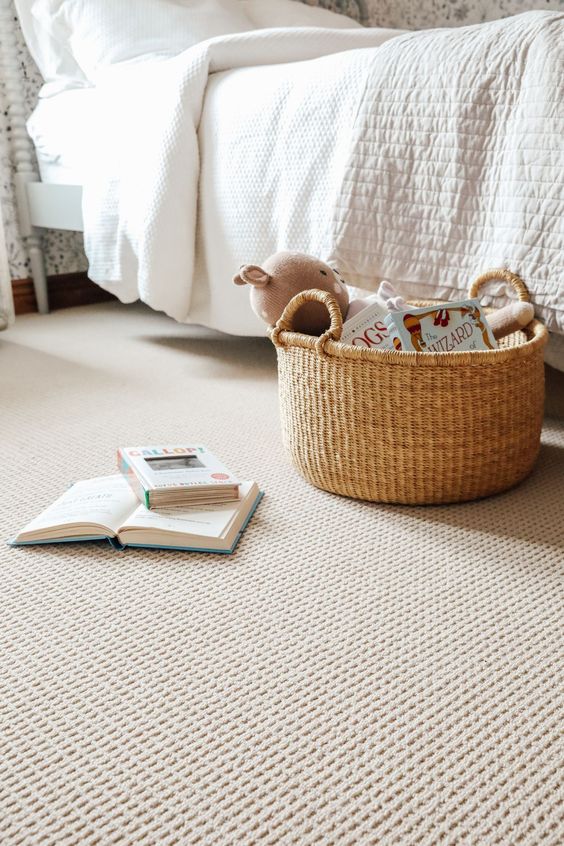 Cozy bedroom scene with a basket of stuffed toys and books beside an open book on the carpeted floor.