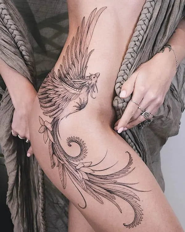 Intricate phoenix tattoo design on woman's side hip, detailed with feathers and floral elements, showcasing artistry.