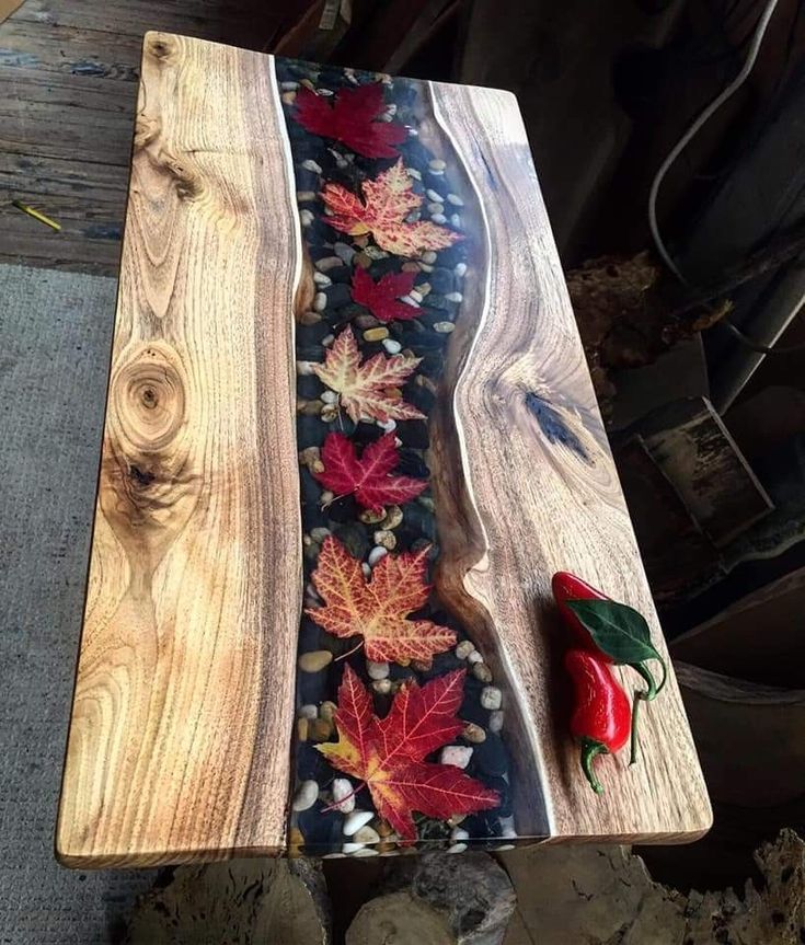 Handcrafted wood table with resin river incorporating autumn leaves and stones, topped with decorative red chilies.