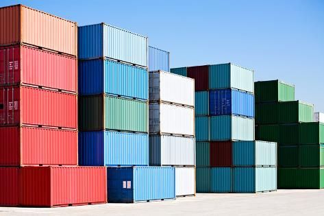 Stacked colorful shipping containers at a port under a clear blue sky.