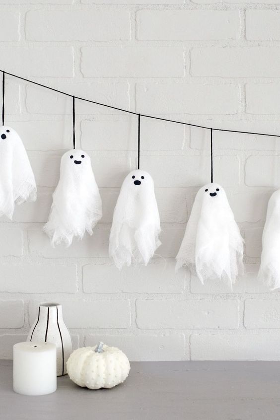 Halloween ghost decor with smiling cheesecloth ghosts hanging on a string over a table with candles and a pumpkin.