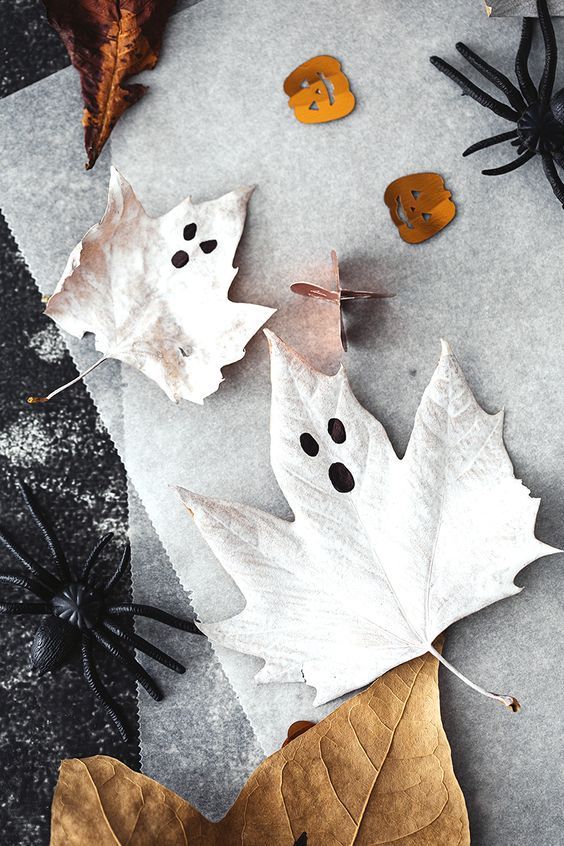 Spooky autumn leaf art with black spiders and pumpkin confetti on parchment paper, perfect for Halloween decorations.