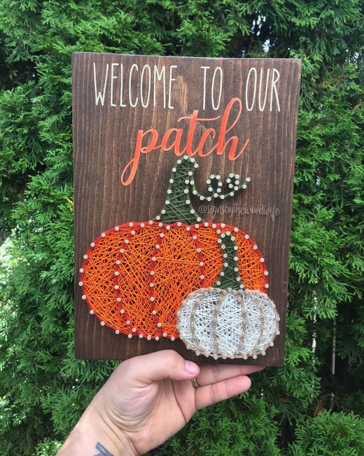 Welcome to Our Patch sign with colorful string art pumpkins held in hand against green foliage background.