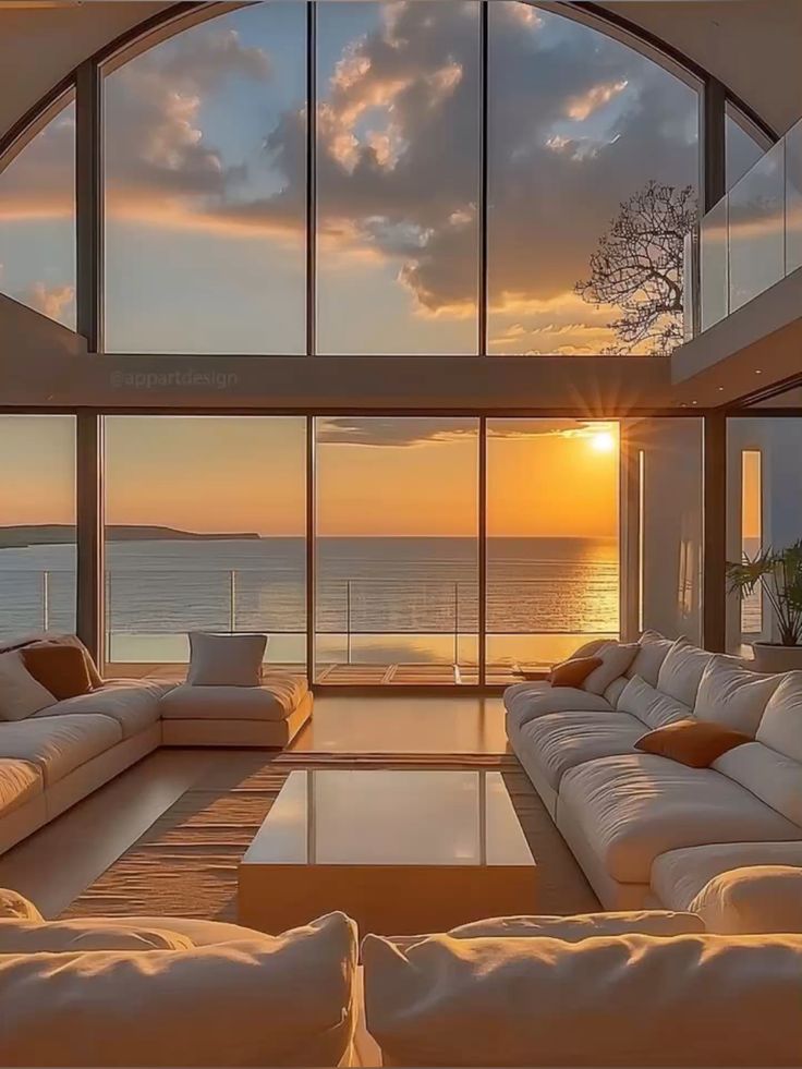 Luxurious living room with ocean view, large windows, sunset, and modern white sofas.