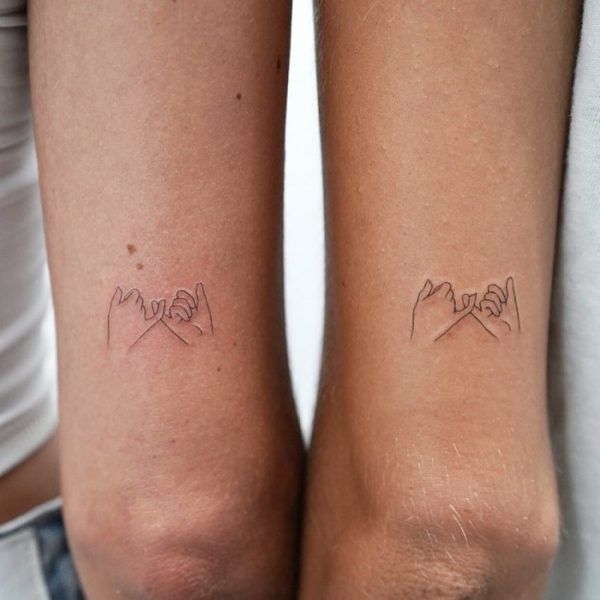 Minimalist matching tattoos of linked pinky fingers on forearms symbolize friendship or promise. Perfect for bonding.