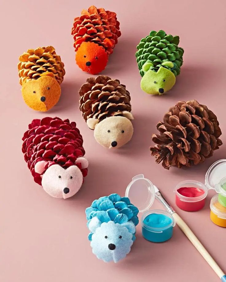 Colorful pinecone hedgehog crafts with paint and brush on a pink background. Ideal for kids' DIY art projects.