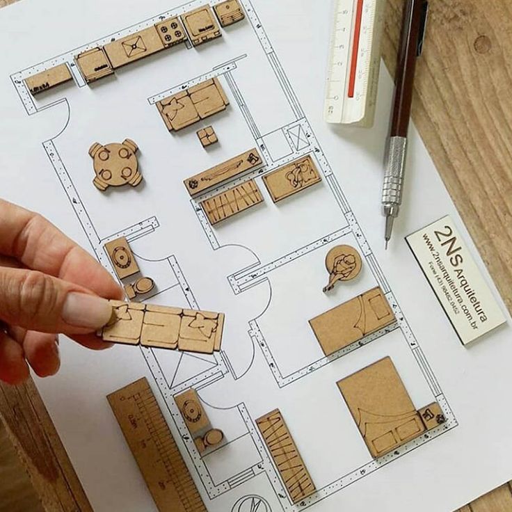 Miniature model furniture arranged on a floor plan, with ruler and pen nearby, showcasing architectural design.