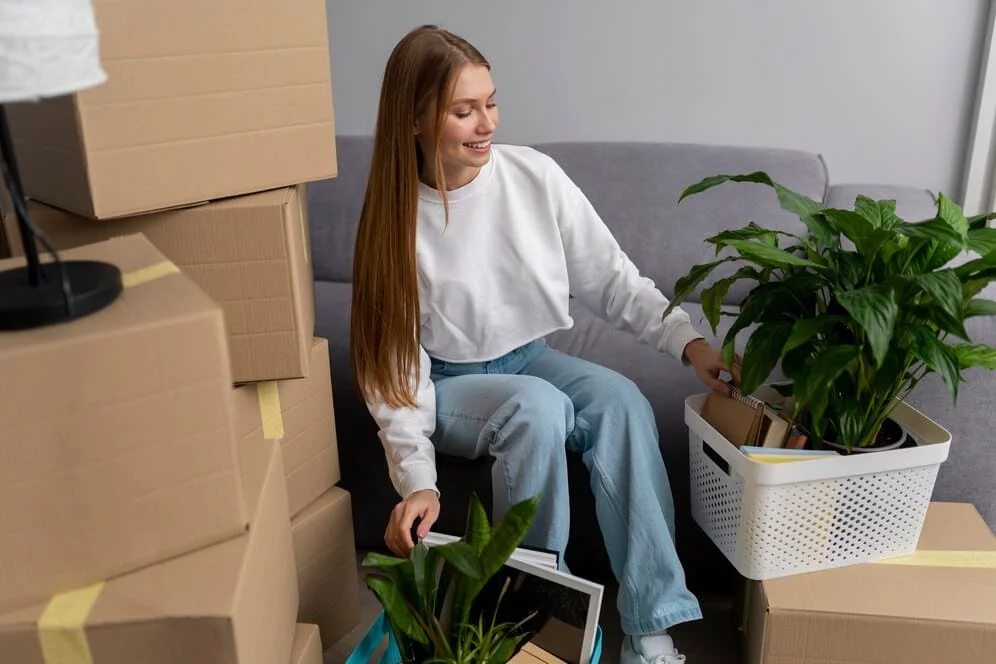 Woman smiling while unpacking boxes and plants in a new home.