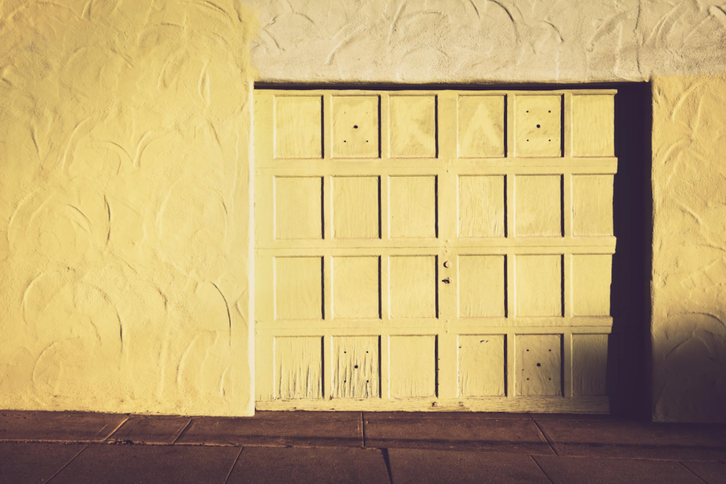 Yellow textured garage door with sunlight casting shadows, closed, surrounded by stucco walls.