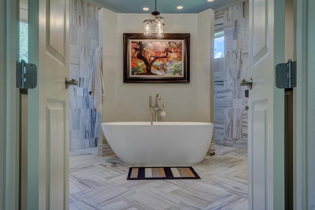 Modern bathroom with a freestanding tub, marble tiles, and nature painting, viewed through open double doors.