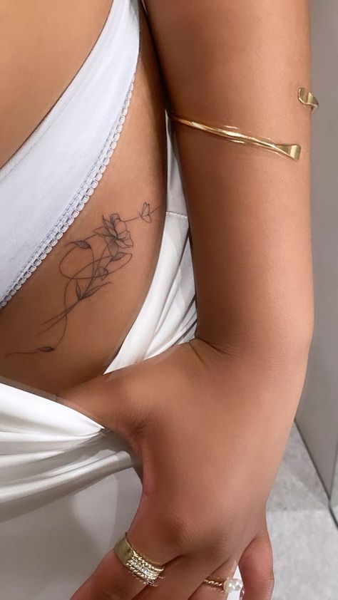 Elegant line art tattoo on side of woman wearing white top, accessorized with gold bangles and rings.