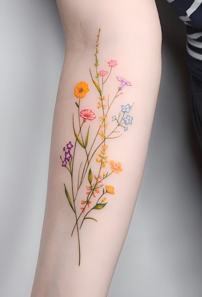 Colorful floral tattoo on forearm with delicate flowers in shades of pink, purple, orange, and blue on light skin.