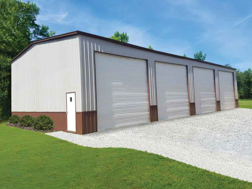 Large metal storage building with four roll-up doors and gravel driveway, surrounded by greenery under a clear sky.