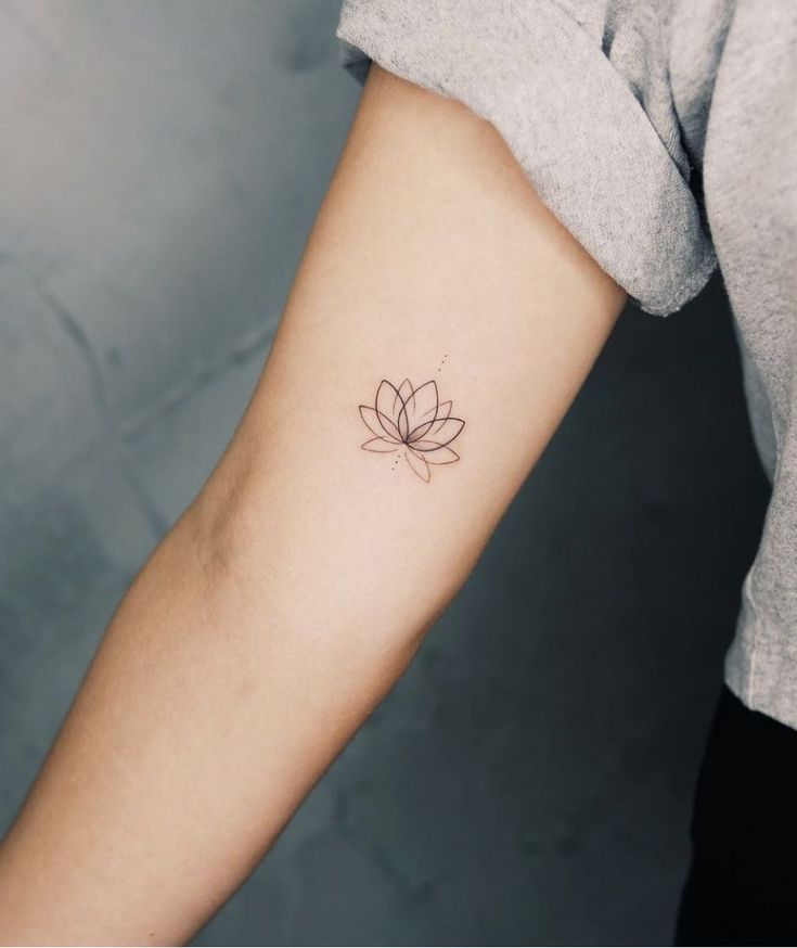 Minimalist lotus flower tattoo on forearm, gray background.