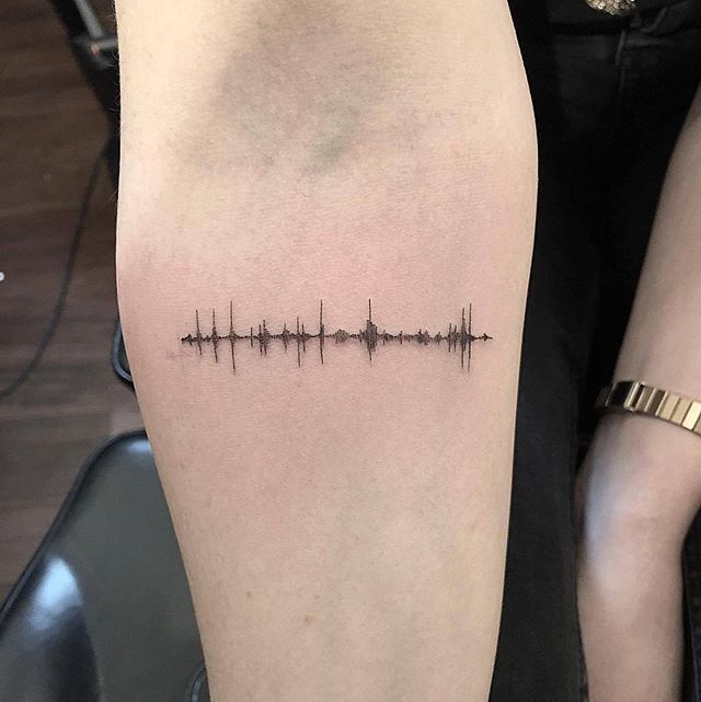 Minimalistic sound wave tattoo on forearm, black ink design.