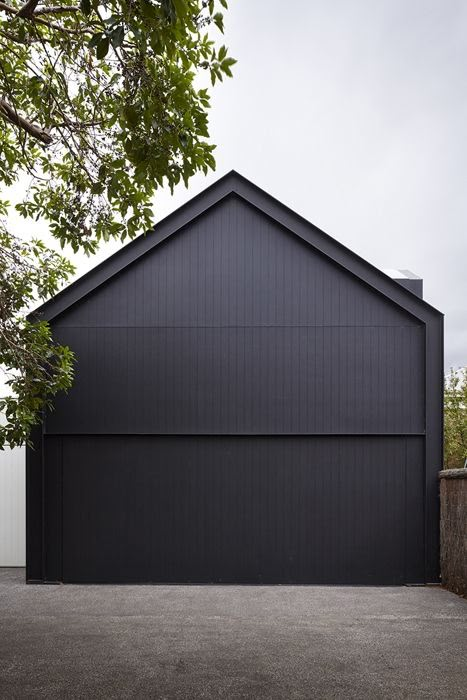 Modern black house facade with sloped roof, surrounded by trees, against a cloudy sky background.