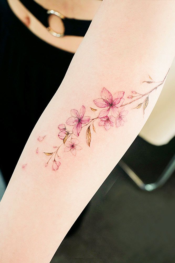 Delicate cherry blossom tattoo on forearm, featuring pink flowers and green leaves, showcasing elegant floral design.