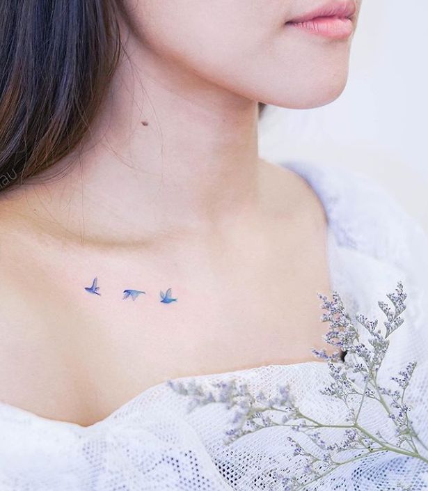 Delicate birds tattoo on woman's collarbone, paired with lavender flowers, showcasing minimalist body art.