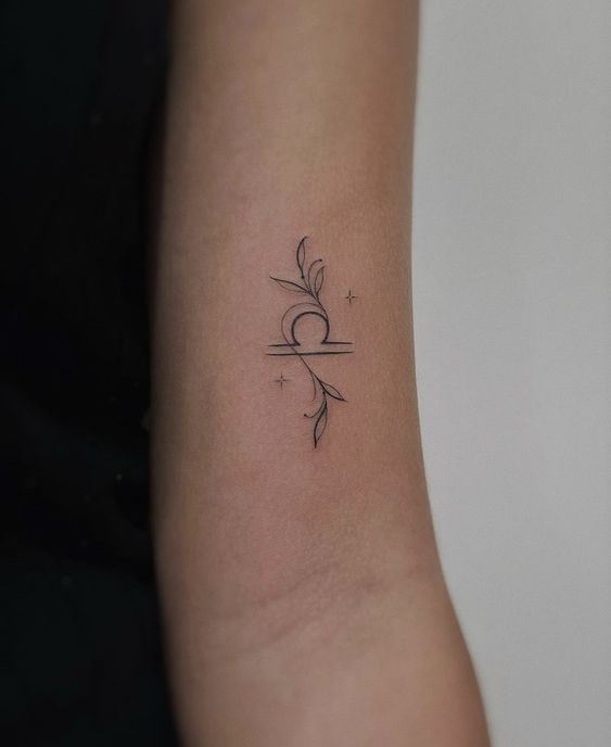 Minimalist Libra tattoo with floral design on forearm, elegant black ink line art.