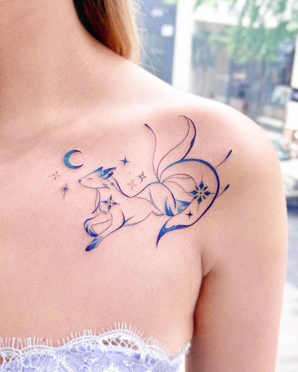 Minimalist blue fox tattoo with moon and stars on woman's shoulder.