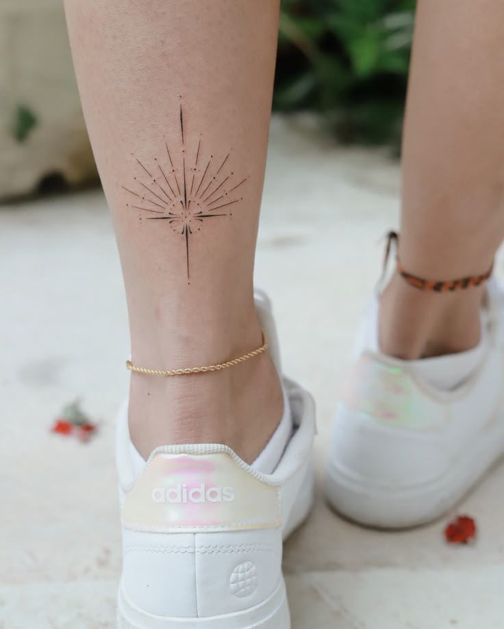 Delicate line tattoo on ankle with gold anklet, wearing white Adidas sneakers.