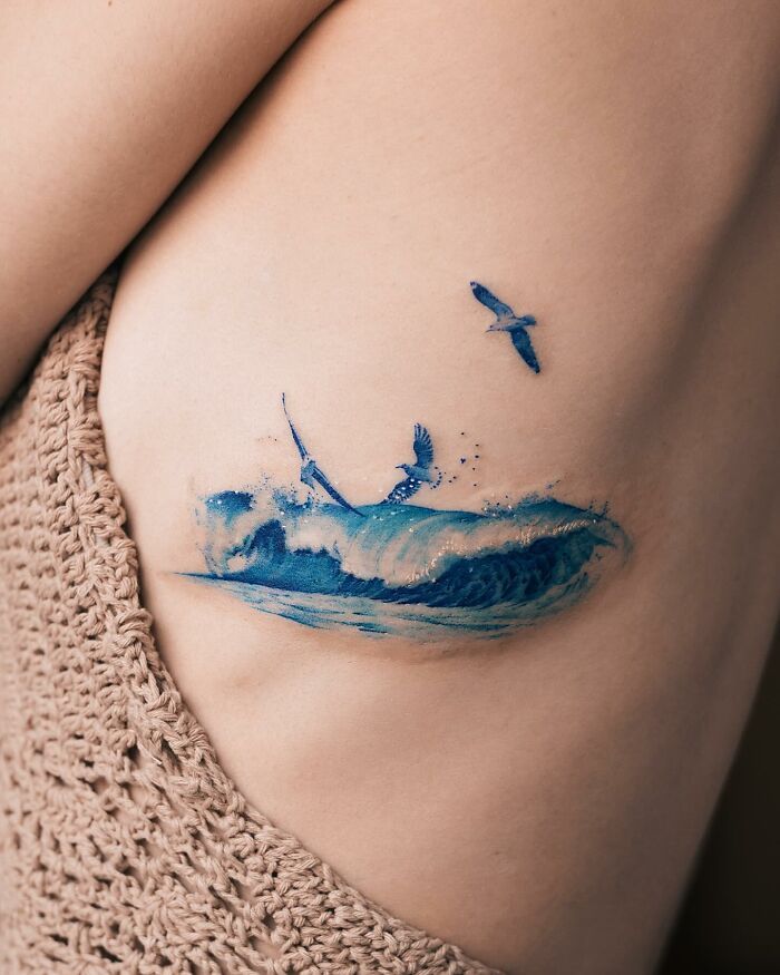 Blue wave tattoo with flying bird on arm, artistic design, detailed and vibrant.