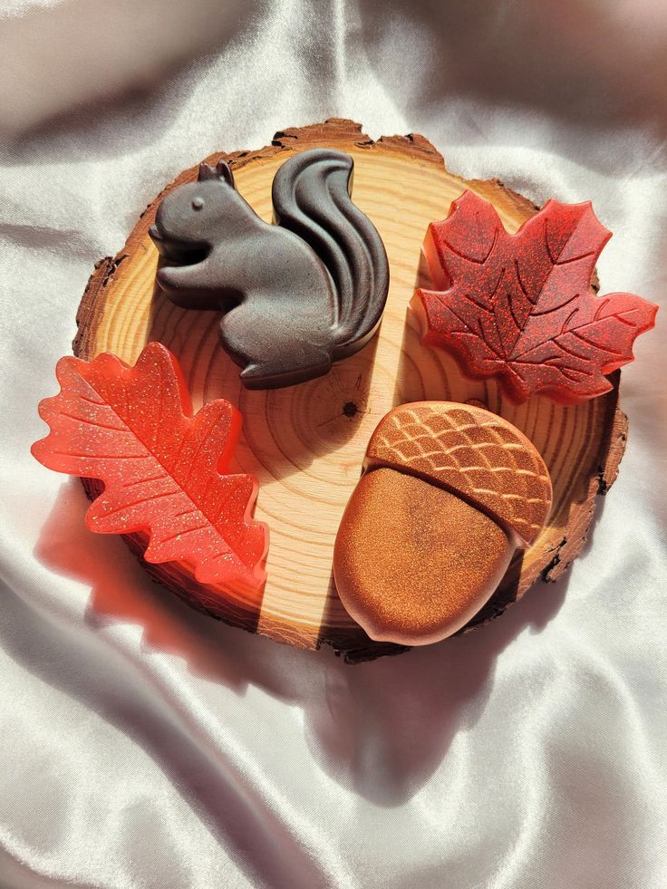 Autumn-themed soaps: squirrel, acorn, and leaves on a wooden slab with a satin background, bathed in warm light.