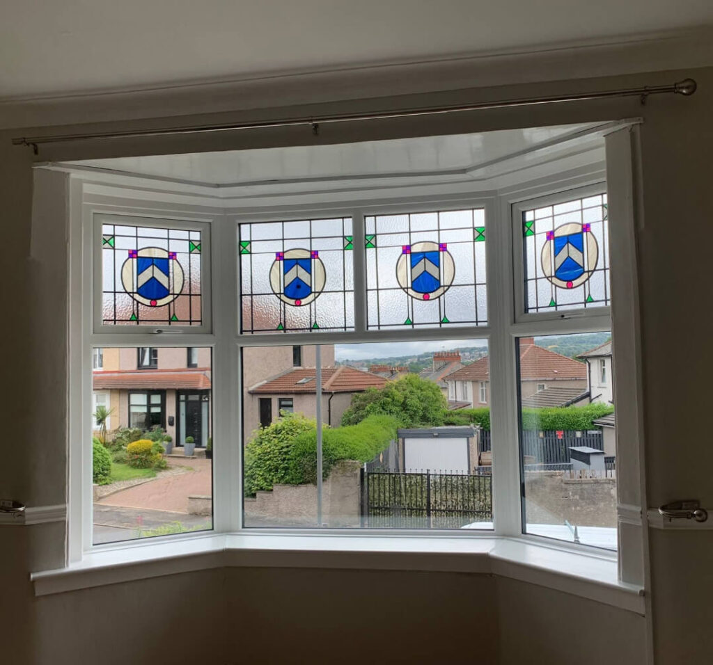 Stained glass bay window with geometric designs overlooking a suburban street with houses and greenery.