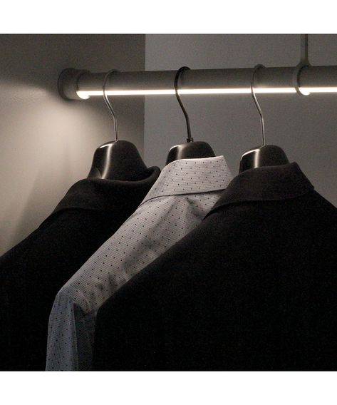 Three neatly hung dress shirts on hangers, featuring two black shirts and one white with dots, in a well-lit closet.