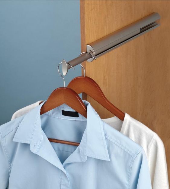 Clothes hanging on a pull-out closet bar, featuring a blue button-up shirt and white garment on wooden hangers.