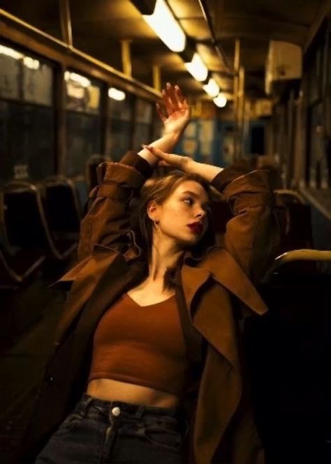 Young woman in a stylish coat poses elegantly on an empty bus at night, creating a moody, cinematic atmosphere.