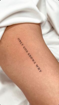 Minimalist tattoo on arm with the phrase Only God Knows Why in black ink, against a background of white fabric.