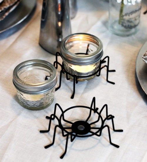 Spider-shaped candle holders with glass jars on a table setting.