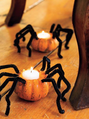 Halloween pumpkin candle holders with spider legs on wooden floor.