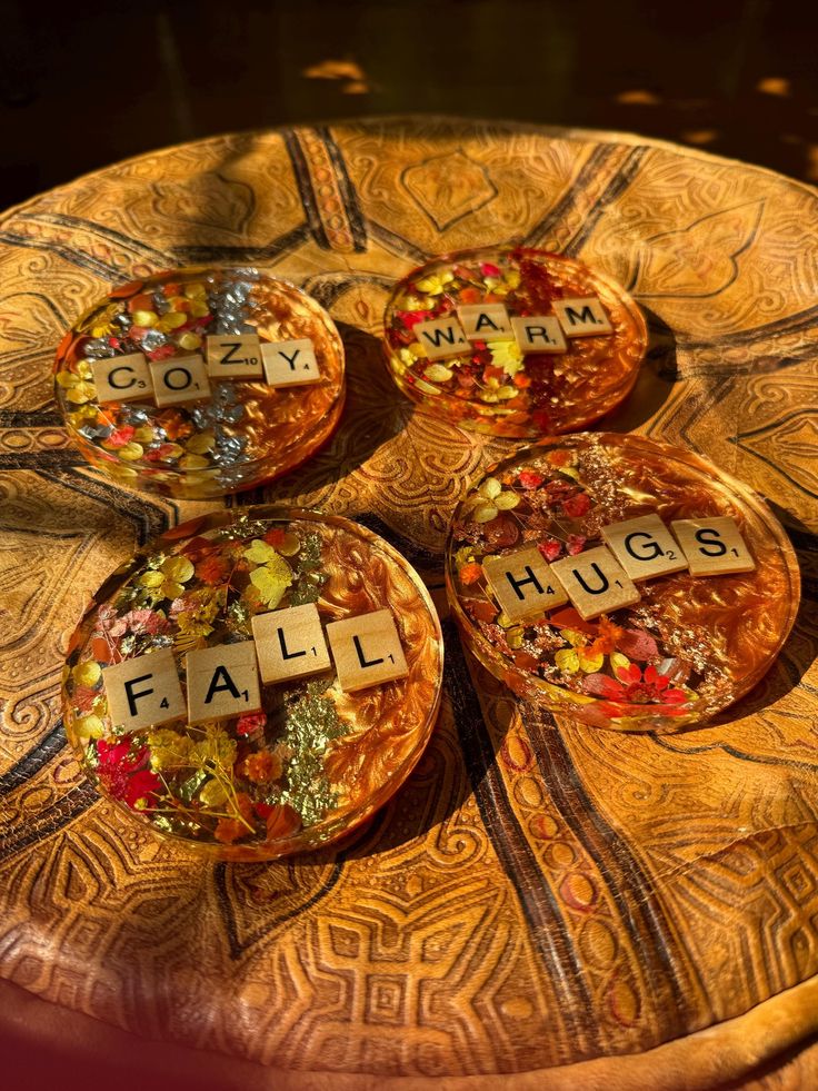 Scrabble tiles forming Cozy Warm Fall Hugs on decorative coasters with autumn leaves, on a wooden table.