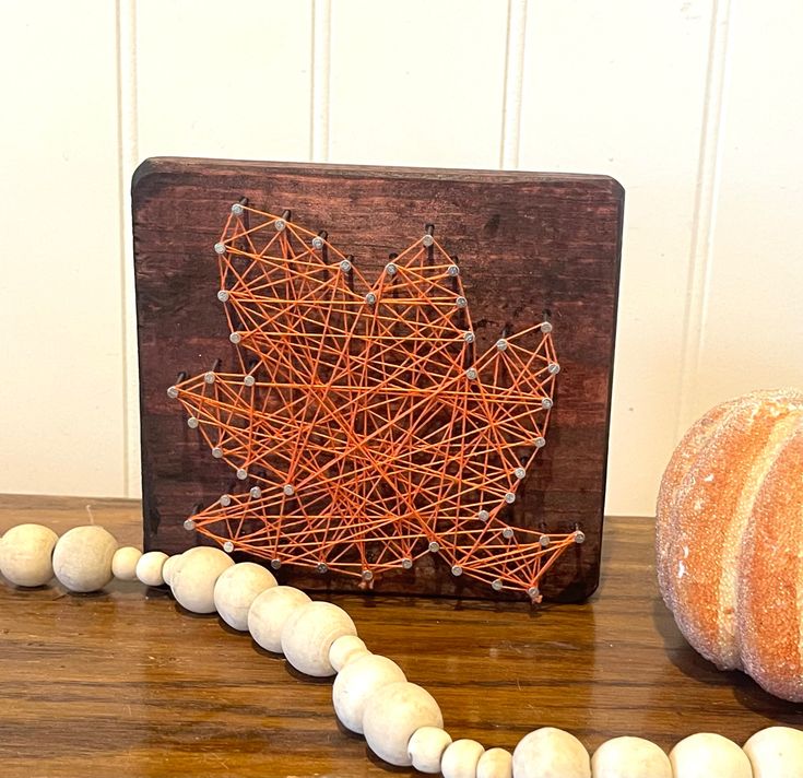 Rustic fall decor: orange string art leaf on wood with autumn accents.